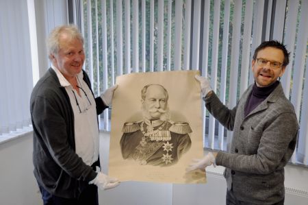 In seinem Namen mussten die Männer aus dem Paderborner Land 1870 in den Krieg gegen Frankreich ziehen. Die Wewelsburger Ausstellungskuratoren Markus Moors (l.) und Andreas Weiß mit einem Porträt des preußischen Königs Wilhelm I., der 1871 zum Deutschen Kaiser proklamiert wurde. (©Kreismuseum Wewelsburg)